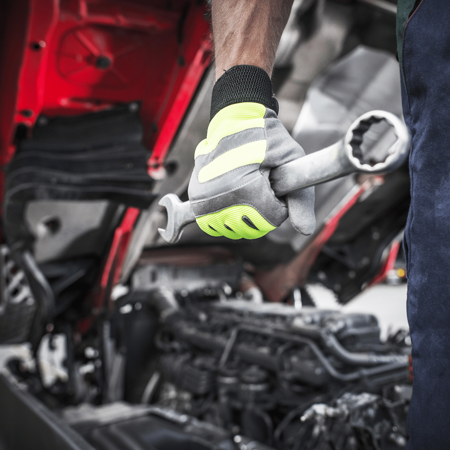 Huoltokorjaaja seisoo tyokalu kadessa, takana korjattava auto pelti avoinna.